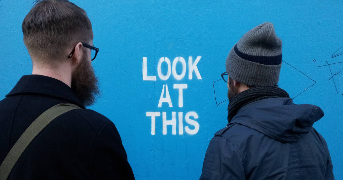 A photo of two guys looking at some graffiti telling them to look at it, kinda like how imposter syndrome tells you to spend all your time focusing on it.